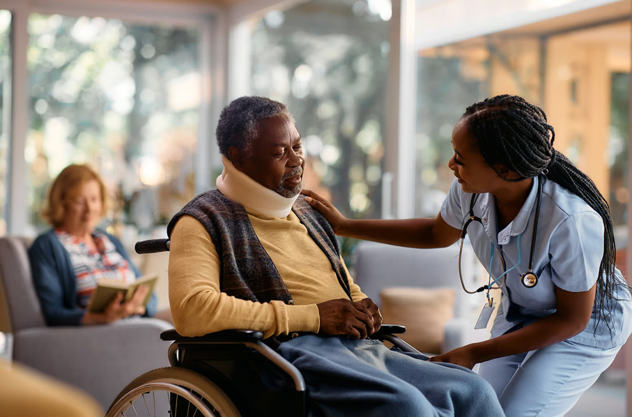 Female healthcare worker supporting a senior resident in a wheelchair at a nursing facility.