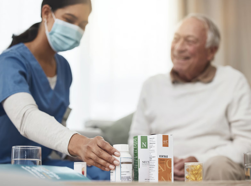 A female home nurse wearing a mask organizing prescription medicine bottles for a smiling senior man.